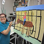 Woman holding a paintbrush in front of a large painting of a horseback rider and horse
