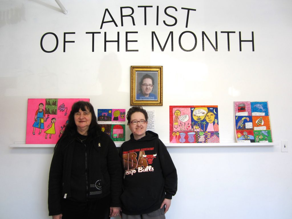 Two Women standing in front of a wall with four drawings